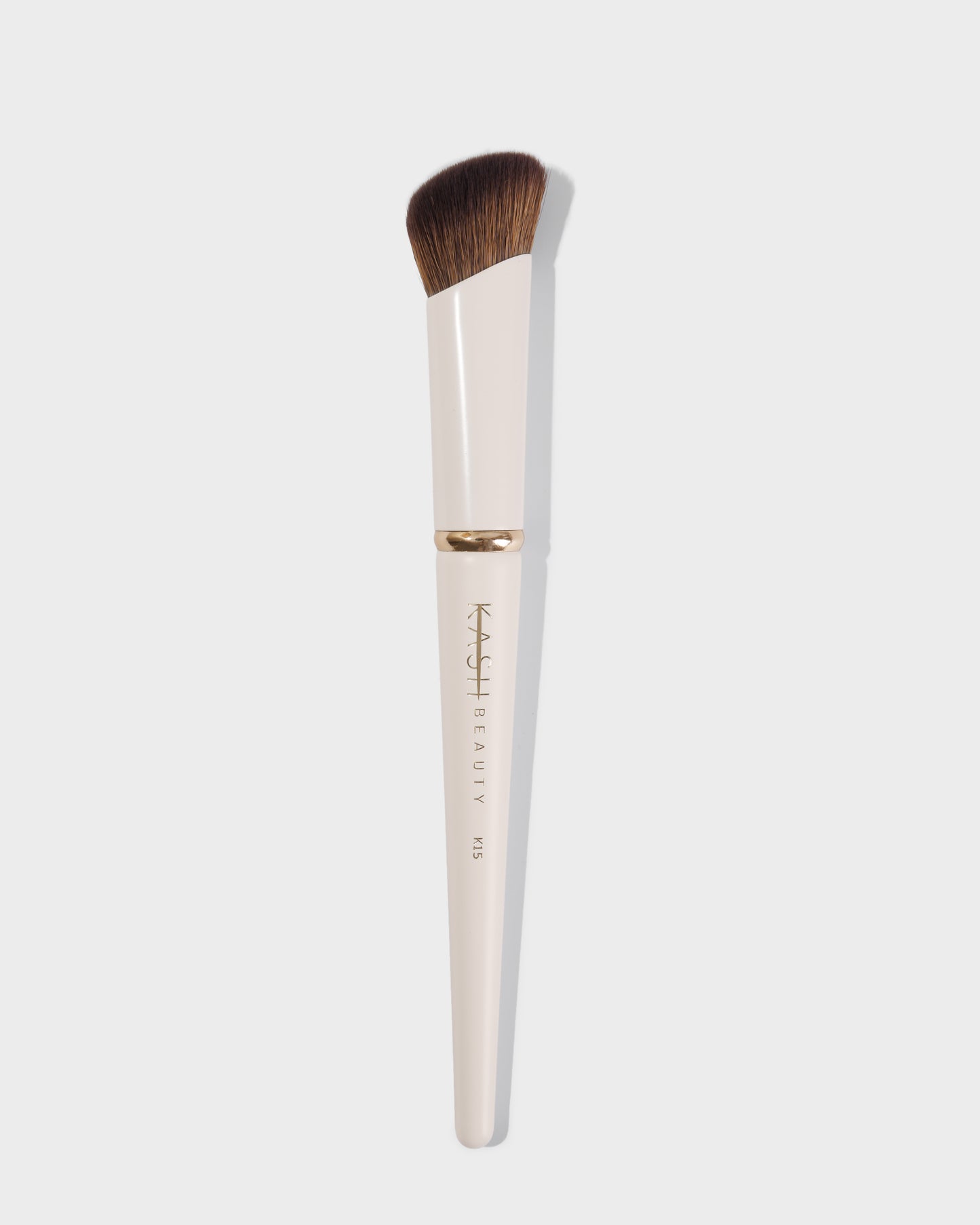 Angled concealer brush with cream handle and soft brown bristles on white background