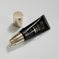 A black cosmetic squeeze tube with gold lettering and a matching metallic gold cap, photographed on a clean light gray studio background.