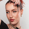 Woman applying a Kash Beauty mascara and holding a mascara tube against a neutral background