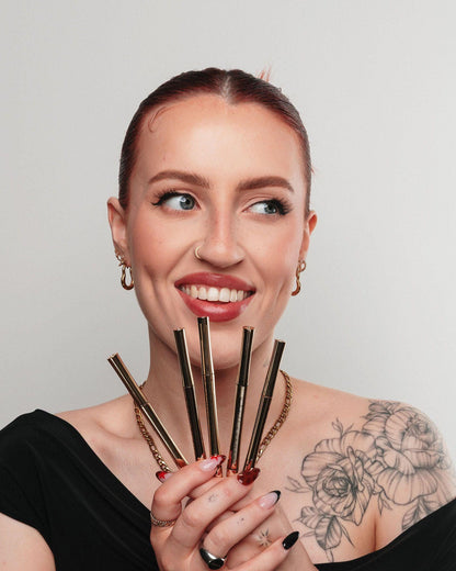 Woman holding five gold Kash Beauty Brow Pencils against a plain background