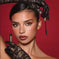 Woman with bold eye makeup holding mascara wand, wearing black lace gloves, red background