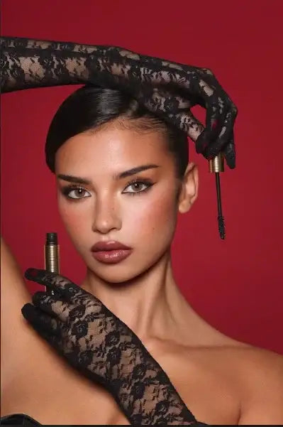 Woman with bold eye makeup holding mascara wand, wearing black lace gloves, red background