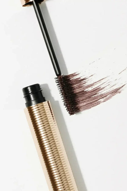 Brown mascara tube with textured gold casing and brush showing color swatch on white background