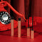Two metallic gold mascara tubes with brushes open on a red background beside a vintage red phone.
