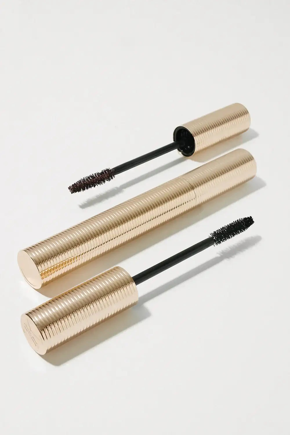 Two gold mascara tubes with textured lids and open wands on a light background
