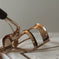 Gold metal eyelash curler with black handle on white book, beauty tool close-up