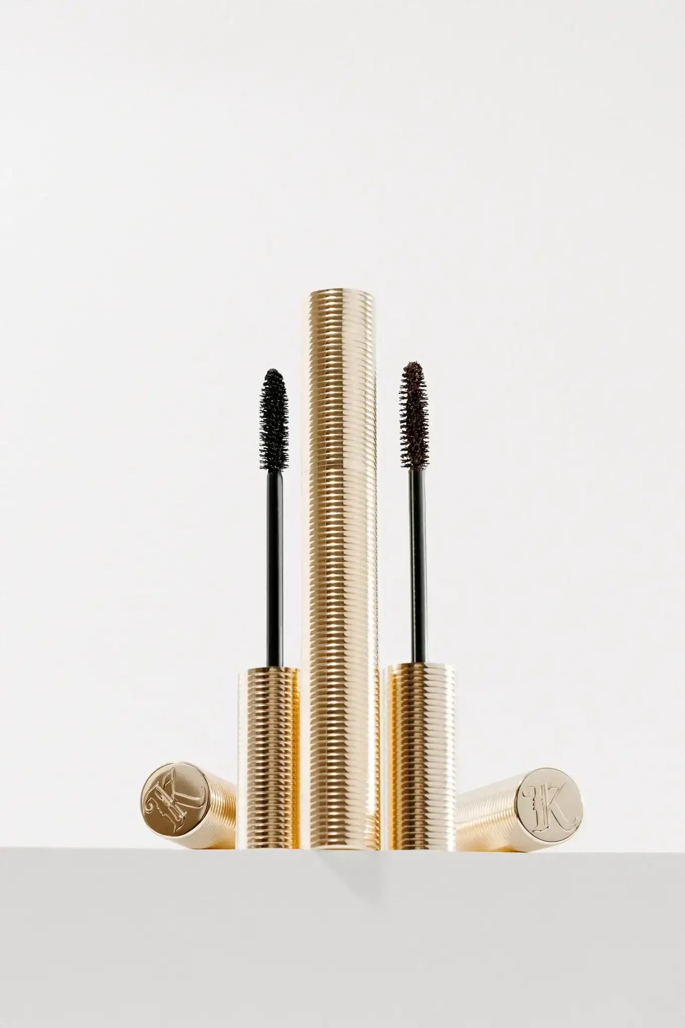 Two gold mascara tubes with textured cases and black and brown wands on white background