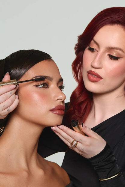 Makeup artist applying mascara to model with flawless glam makeup and defined brows