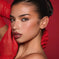 Woman with flawless makeup, winged eyeliner, and glossy lips, posing in red gloves against a red background