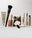 Makeup set with primer, foundation, powder, concealer, mascara, and brushes on white background.