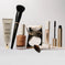 Makeup set with primer, foundation, powder, concealer, mascara, and brushes on white background.