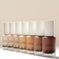 Aura Skin Radiant Foundation bottles in assorted skin tone shades, arranged in a row