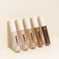 Five liquid concealers in different shades lined up on a beige background